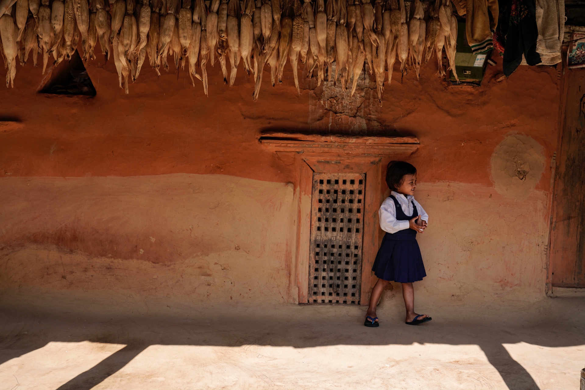 A young girl in school uniform outside a traditional Nepali home